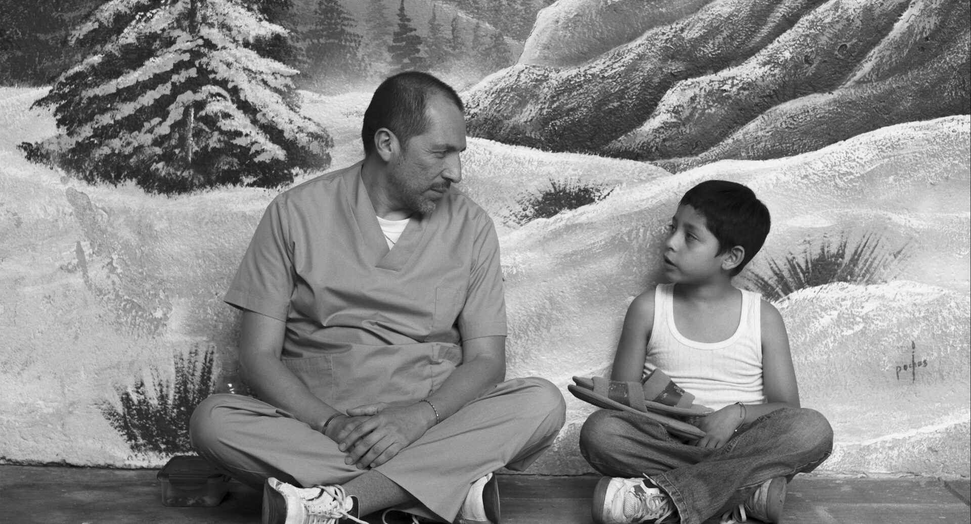 Der Vater in Krankenhauskleidung und der Junge sitzen vor einer gemalten Schneelandschaft